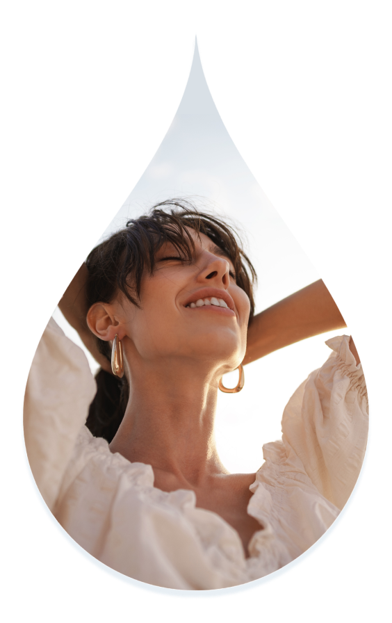 A smiling woman on the beach looking towards the sky. Image is in the shape of a droplet.